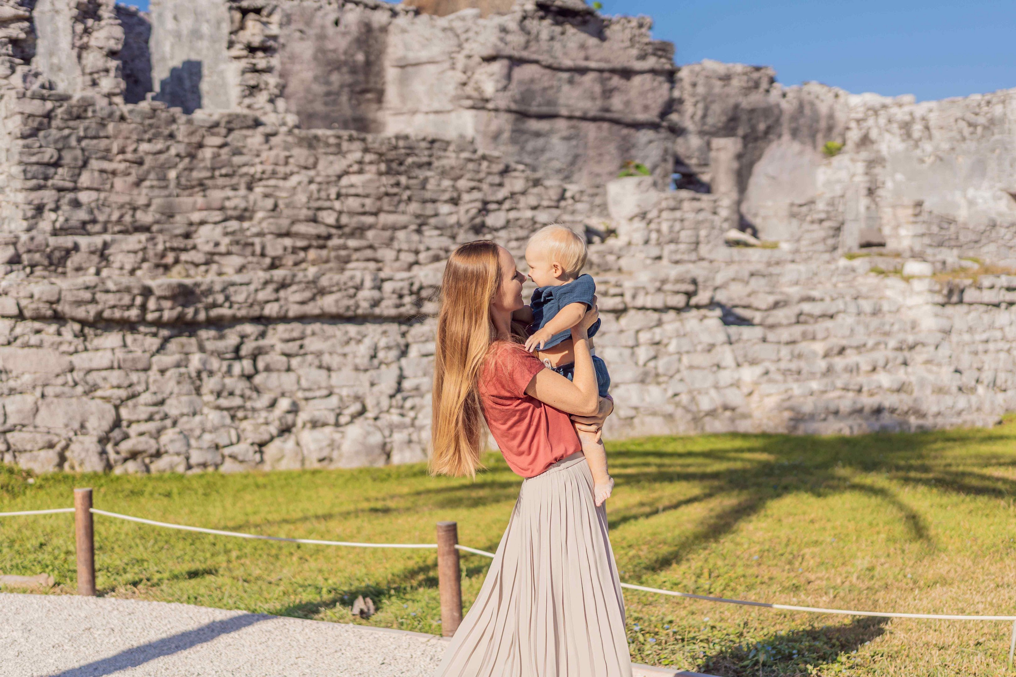 Mom holds her child with Mexican ruins in the background on Mexican Mother’s Day.