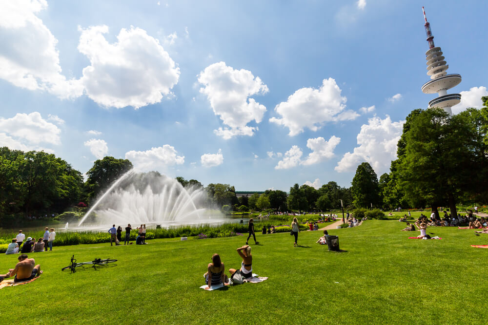 Menschen auf einer Wiese mit See und Wasserspielen in Planten un Blomen in Hamburg.