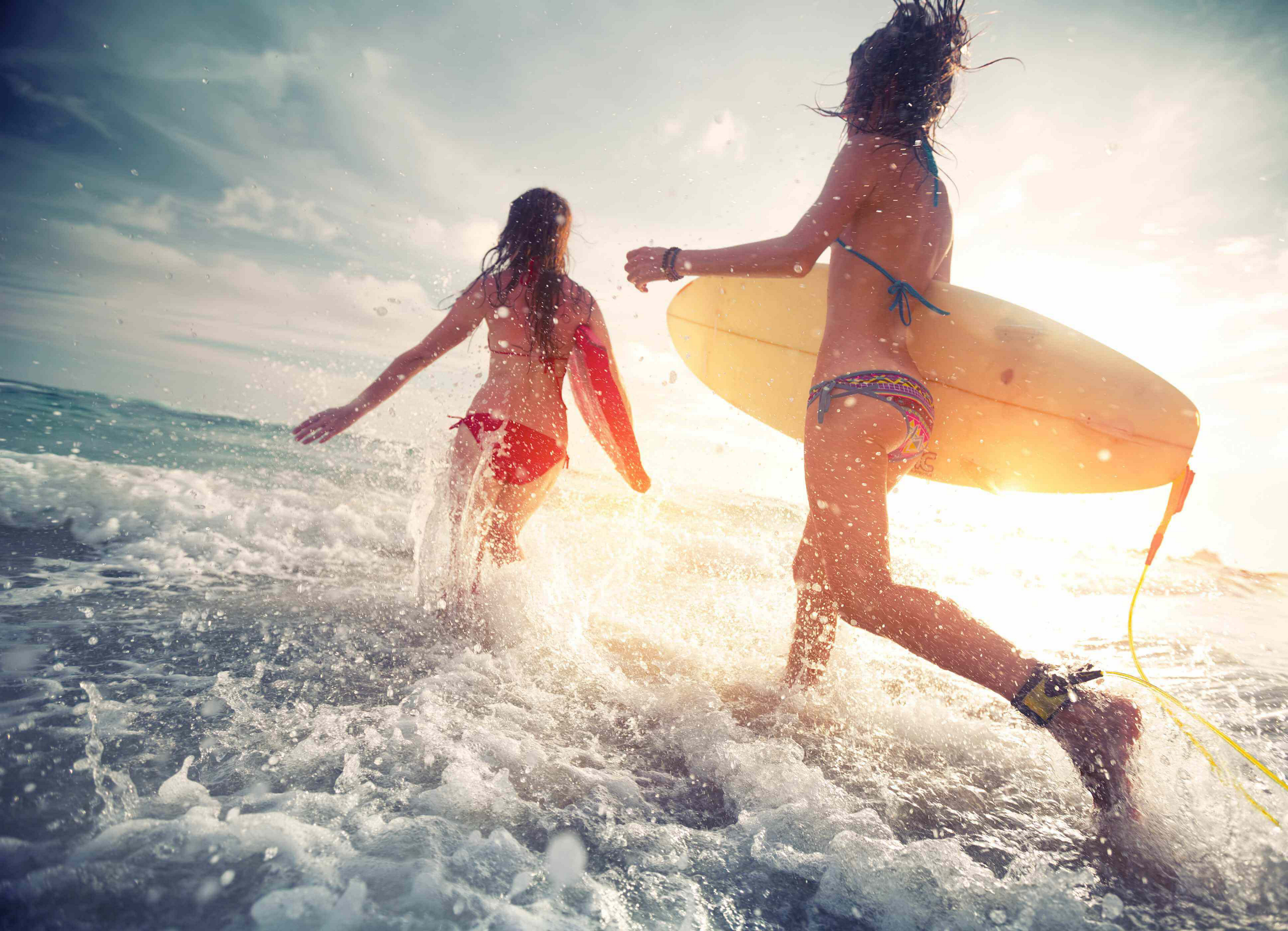 Zwei Frauen laufen mit Surfbrettern ins Wasser